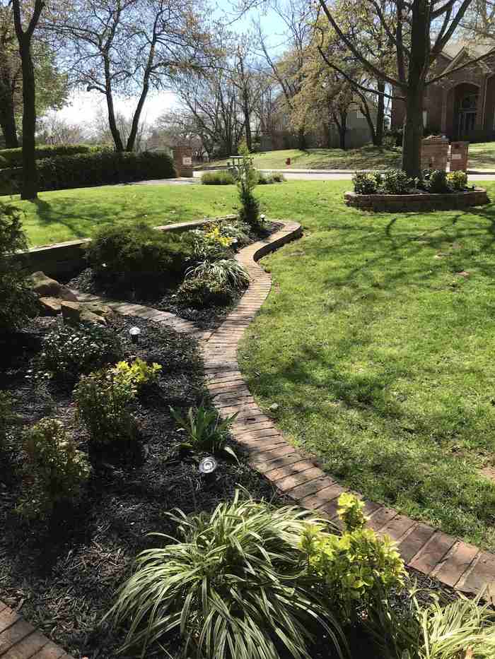 Curved brick garden path bordered by planted beds and a green lawn.