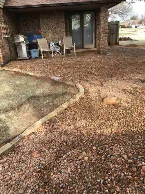 Rock-covered yard with a fieldstone edge beside a covered patio.